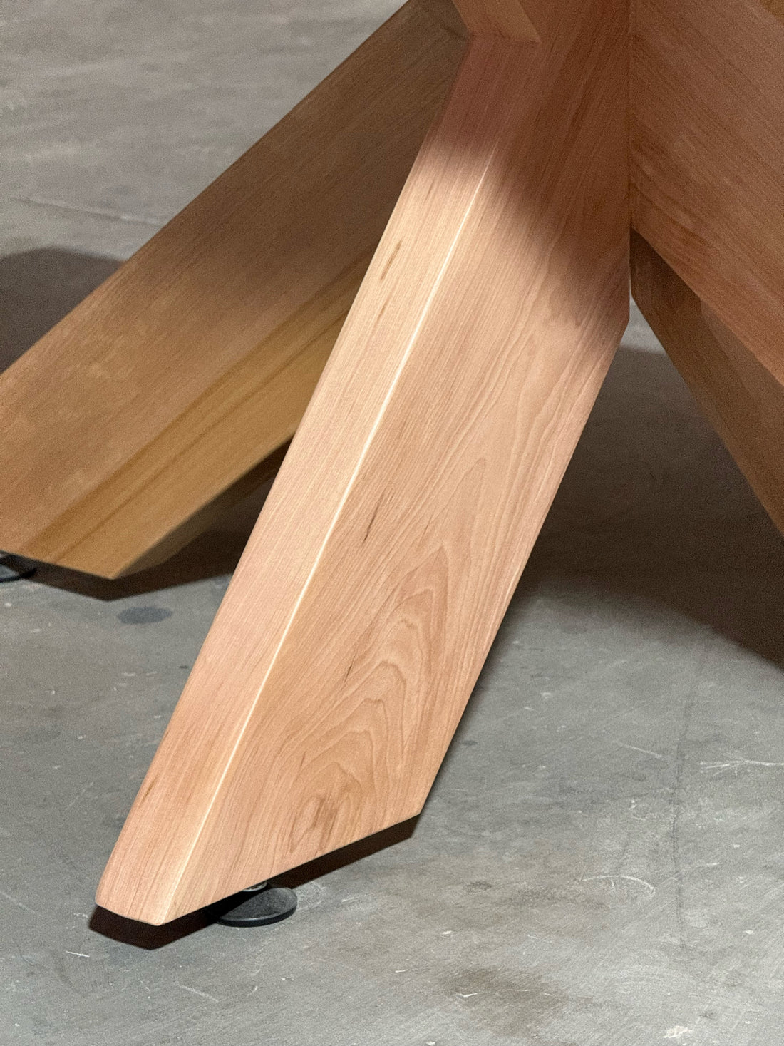 Detalle de una pata de lenga maciza de la mesa de comedor rectangular Lena, con su patín nivelador regulable.
