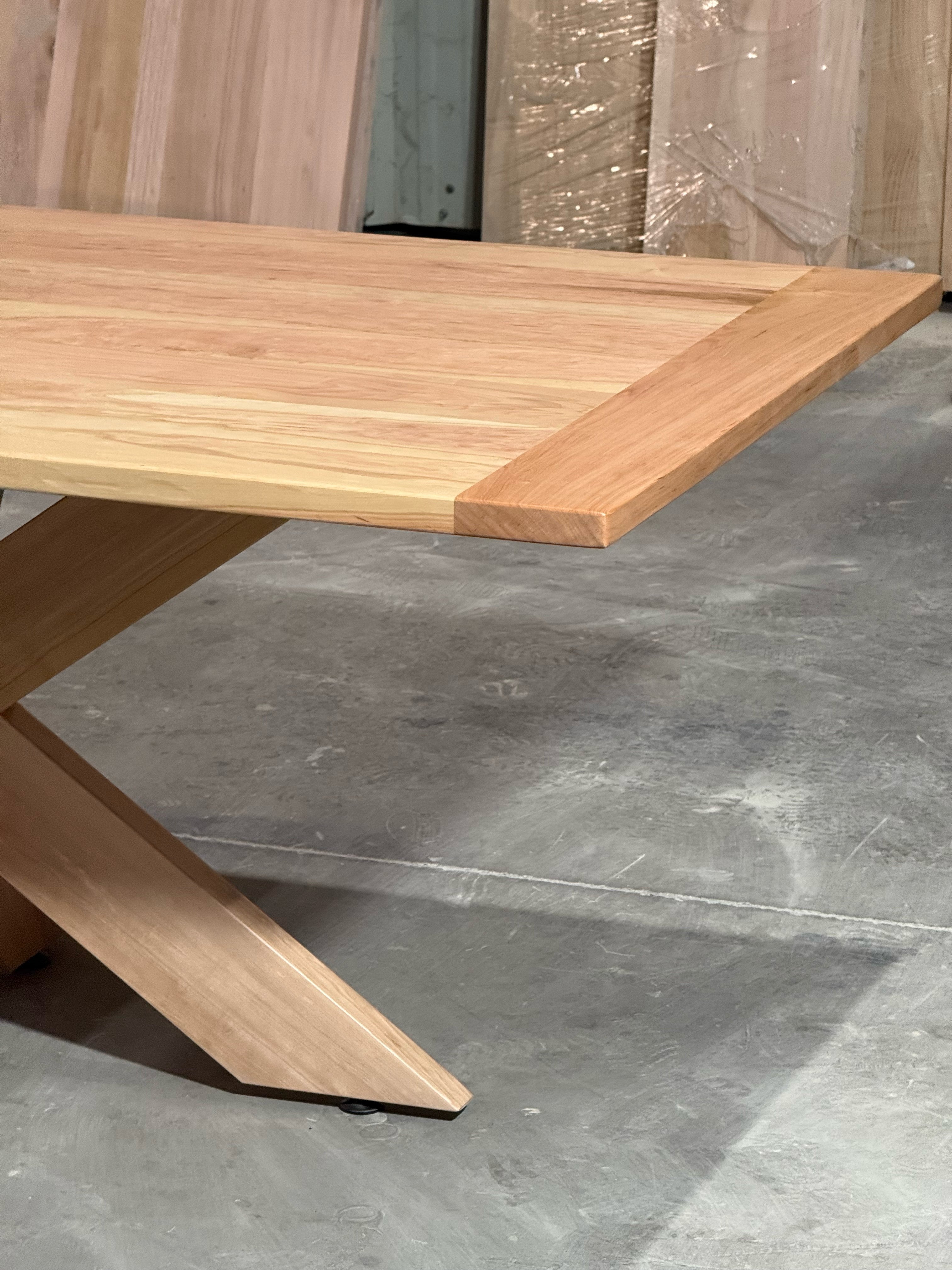 Extremo de la cubierta de lenga de la mesa de comedor rectangular Lena, con el canto redondeado y una de las patas de la base.