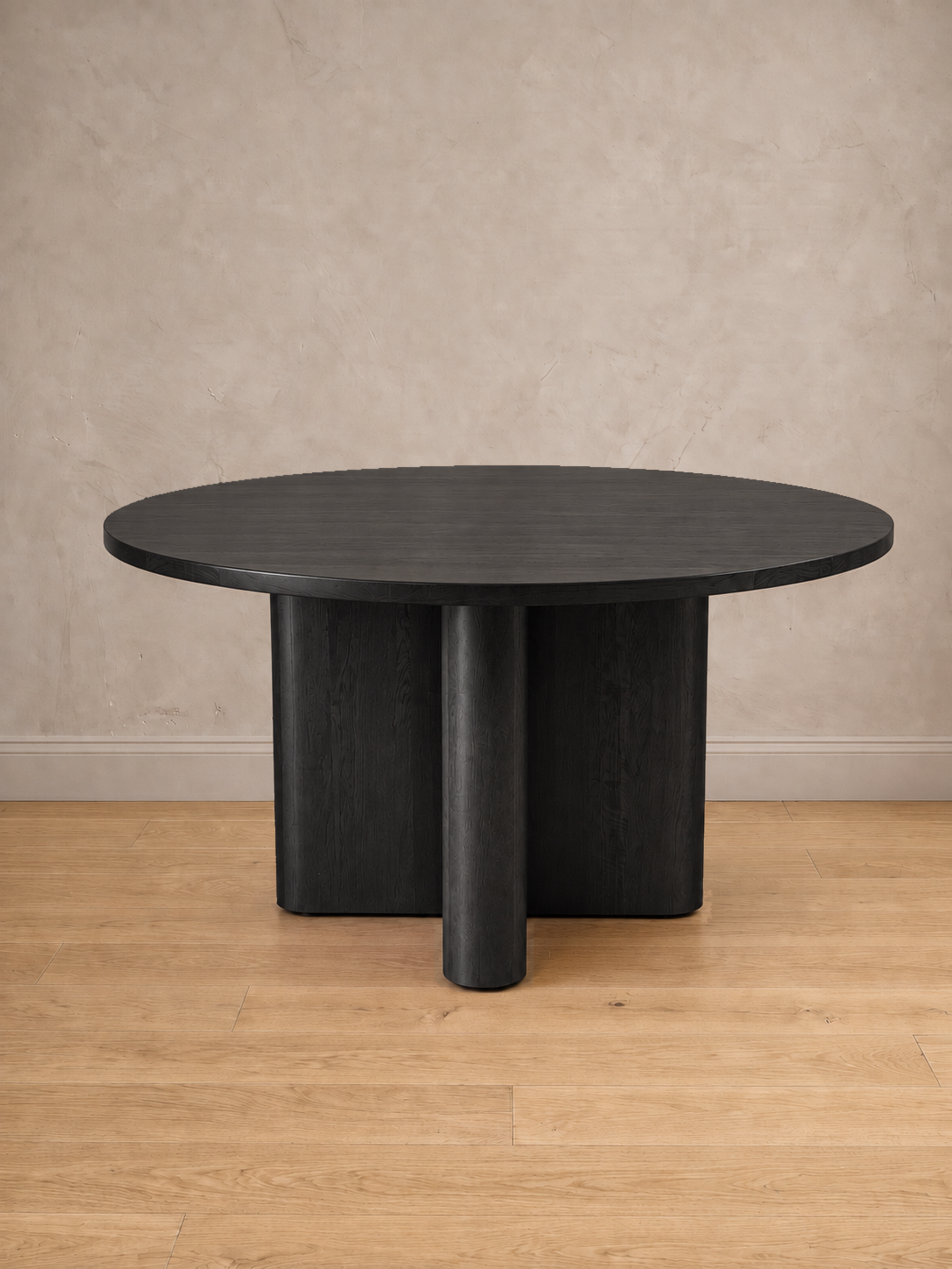 Mesa de comedor redonda Amora en tono negro, con su base en cruz de remates curvos.