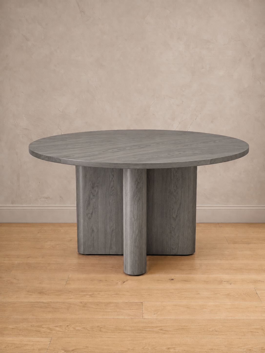 Mesa de comedor redonda Amora en tono gris, con su base en cruz de remates curvos.