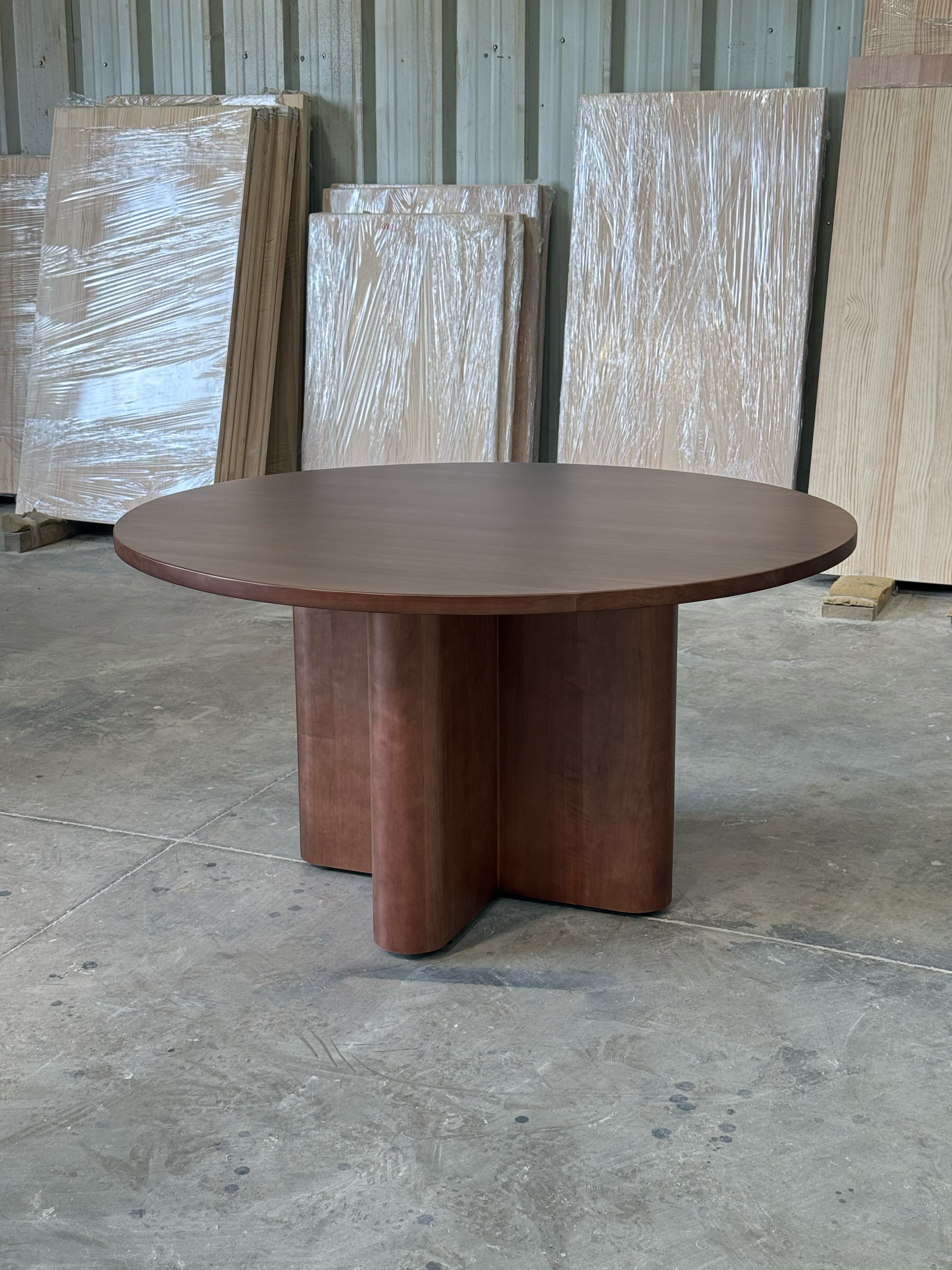Mesa de comedor redonda Amora en lenga tono nogal, vista en tres cuartos con cubierta y base en cruz completas, en el taller de Santino Design.